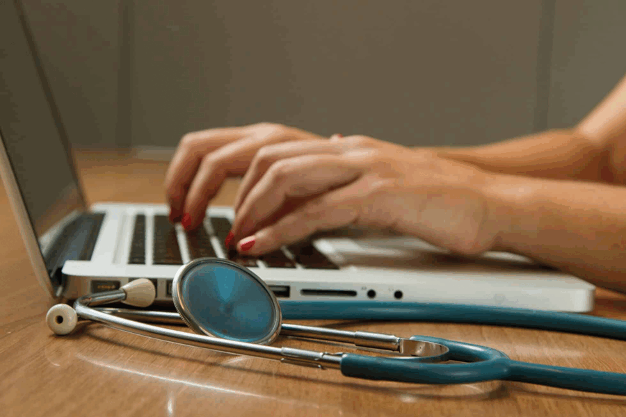 Mains tapant sur un ordinateur, on aperçoit un stéthoscope
